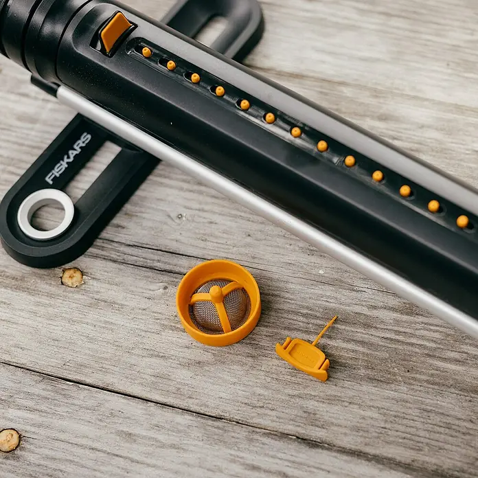 Fiskars Ersatzteil-Set Oszillierende Regner - Passend für: Fiskars X-Series™ Oszillierende Regnern S–L und S–M sowie Comfort Oszillierende Regnern S–L und S–M - Das Bild zeigt einen Fiskars-Rasensprenger mit abnehmbaren Teilen auf einer Holzoberfläche. Das Produkt ist schwarz, silber und orange.