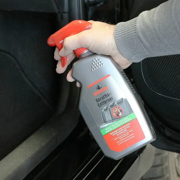 Nigrin Geruchsentferner - 500 ml - Eine Hand hält eine Sprühflasche Nigrin Geruchsentferner, die für die Anwendung im Auto bereit ist.