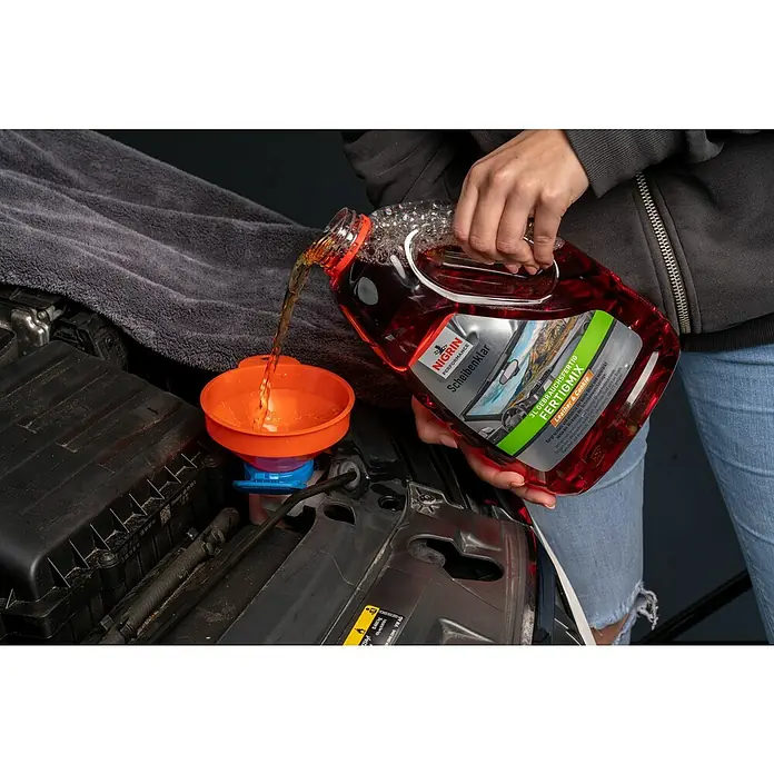 Nigrin Performance Scheibenklar Fertigmix Leather & Cookie - 3 l - Flüssigkeit wird durch einen Trichter in einen Behälter im Motorraum eines Autos gegossen, wahrscheinlich Scheibenwaschflüssigkeit von Nigrin.