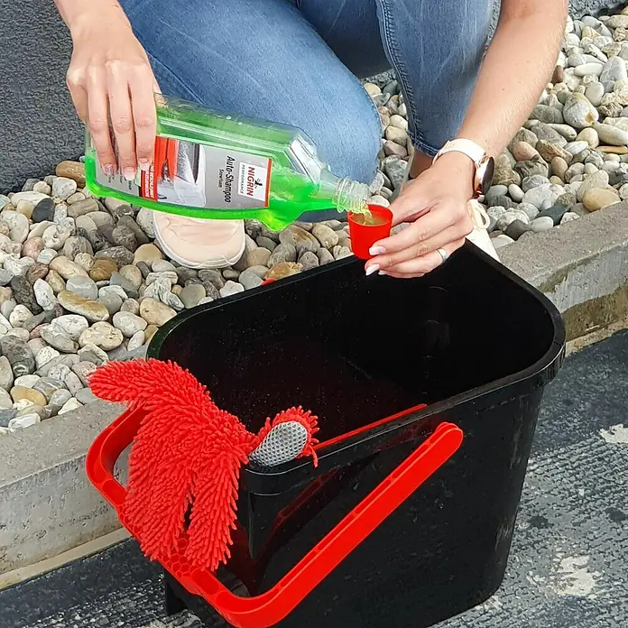 Nigrin Performance Auto-Shampoo Snowfoam - 1 l - Autoshampoo wird in einen Messbecher gegossen, bevor es in einen Eimer mit einem roten Mopp gegeben wird.