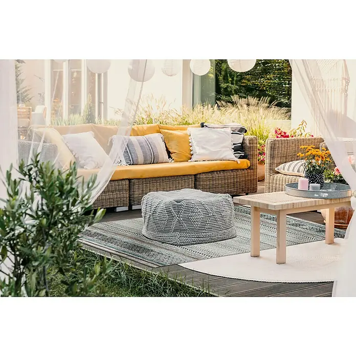 Outdoor-Teppich Austin - Graublau, 230 x 160 cm, 100 % Polypropylen - Gemütliche Sitzecke im Freien mit Rattansofa, Pouf und Holztisch auf einem gemusterten Teppich, ideal zum Entspannen im Garten.