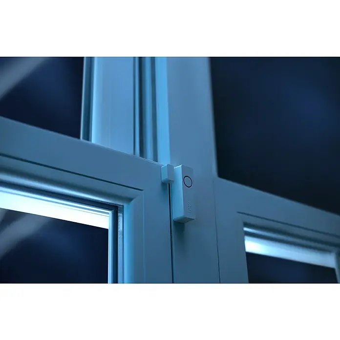 Philips Hue Sensor de ventana y puerta - Blanco, ZigBee, 1 unidad - Primer plano de un sensor de ventana inteligente en un marco de ventana blanco, que garantiza una mayor seguridad. El dispositivo es discreto y moderno.
