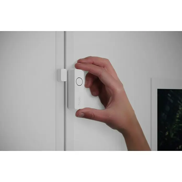 Philips Hue Sensor de ventana y puerta - Blanco, ZigBee, 1 unidad - Una mano instala un sensor de movimiento blanco Philips Hue en un marco de puerta blanco. El sensor tiene un botón y el logotipo de Hue.