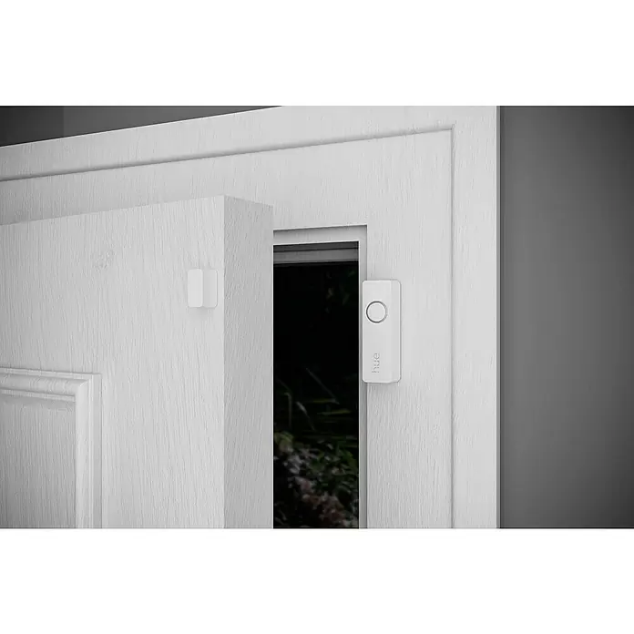 Philips Hue Sensor de ventana y puerta - Blanco, ZigBee, 2 unidades - Primer plano de un sensor de puerta Philips Hue blanco fijado a una puerta blanca, que ofrece domótica inteligente para mayor seguridad.