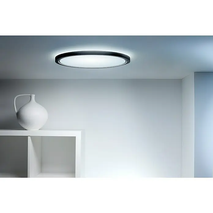 Philips Wiz Smart-LED-Deckenleuchte rund Tunable White & Color SuperSlim - 32 W, Ø x H: 55 x 4,8 cm, Schwarz, RGBW - Ein modernes Zimmer mit einer eleganten runden Deckenleuchte, die ein helles Licht spendet, und einer weißen Vase auf einem Regal.