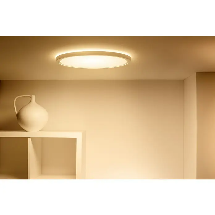 Philips Wiz Smart-LED-Deckenleuchte rund Tunable White & Color SuperSlim - 22 W, Ø x H: 43 x 4,8 cm, Weiß, RGBW - Ein modernes LED-Panel Deckenleuchte beleuchtet einen minimalistischen Raum mit einem Regal und einer weißen Vase.
