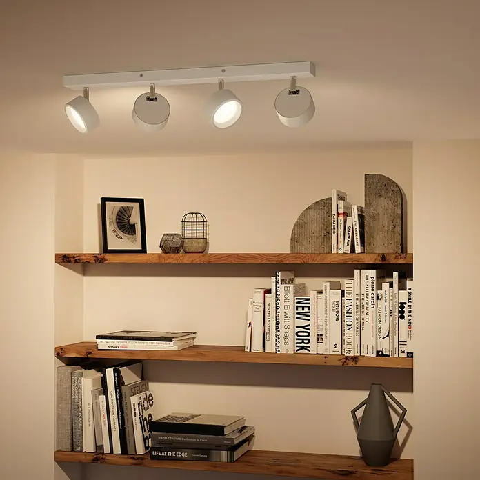 Philips Regleta LED Bracia - 22 W, L x An x Al: 60 x 8 x 12,5 cm, Blanco, Blanco cálido, 4 ud. - Lámpara de techo con cuatro focos en blanco, iluminando una estantería. La luz proporciona una iluminación agradable.
