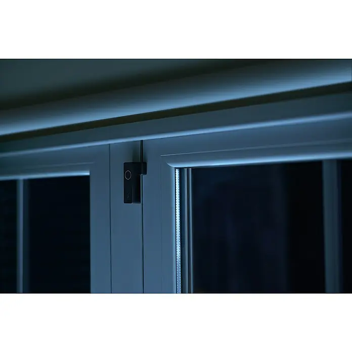 Philips Hue Sensor de ventana y puerta - Negro, ZigBee, 2 unidades - Imagen de un sensor de contacto Philips Hue en un marco de ventana blanco, ideal para el control inteligente de la iluminación.