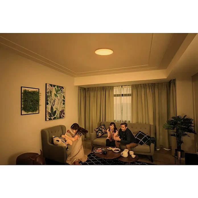 Philips Plafón LED redondo Izso - 24 W, Ø x Al: 34,7 x 6 cm, Blanco, Blanco cálido - Foto interior de una habitación con una lámpara de techo, donde una familia está pasando tiempo. La lámpara emite una luz cálida y acogedora.