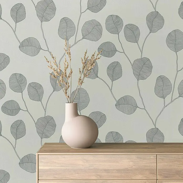 Marburg GZSZ Vliestapete Blätterranke - Grau/Schwarz/Weiß, Floral, 10,05 x 0,53 m - Elegante Tapete mit Eukalyptus-Blattmuster und eine stilvolle Vase mit Trockenblumen auf einer Holzkommode.