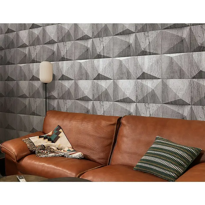 Marburg GZSZ Vliestapete Holzwand - Dunkelgrau, 3D-Optik, 10,05 x 0,53 m - Wohnzimmer mit einem braunen Ledersofa, einer Stehlampe und einer Wand mit einem geometrischen 3D-Holzpaneel-Design.