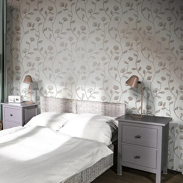 Marburg GZSZ Vliestapete Blumenranke - Grau/Bronze, Floral, 10,05 x 0,53 m - Schlafzimmer mit großem Bett, zwei grauen Nachttischen und floraler Tapete. Die Lampen spenden gemütliches Licht und schaffen eine entspannende Atmosphäre.