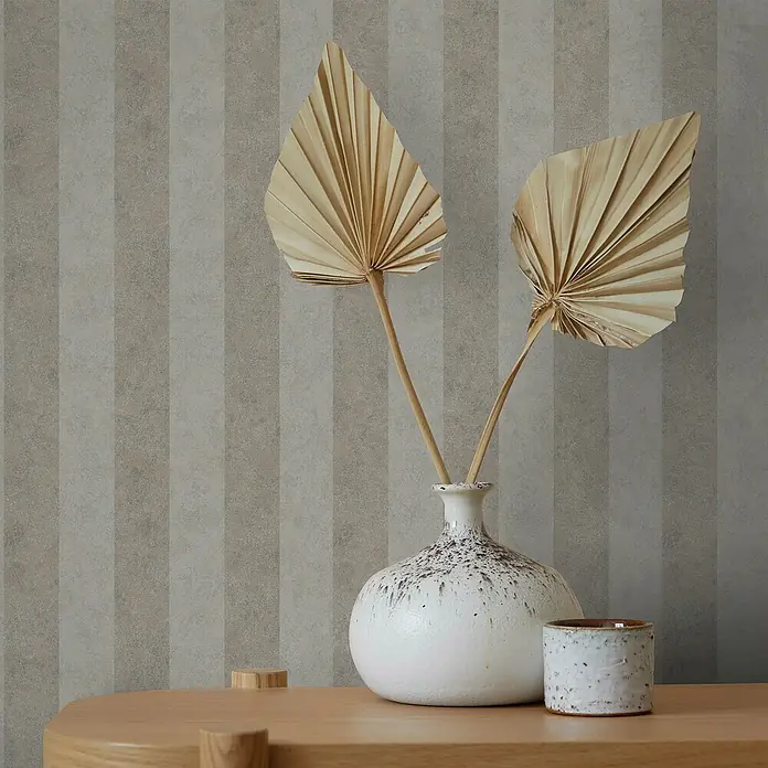 Marburg GZSZ Vliestapete - Braun, Streifen, 10,05 x 0,53 m - Elegante Dekoration mit einer weißen Vase, Trockenblumen und einem Keramikbecher auf einem Holztisch vor gestreifter Tapete.