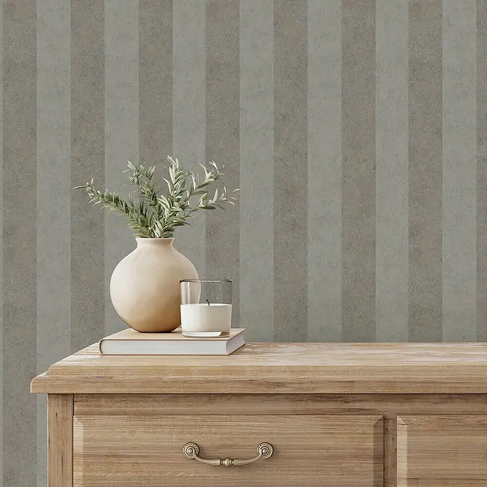 Marburg GZSZ Vliestapete - Braun, Streifen, 10,05 x 0,53 m - Dekorative Nahaufnahme eines Interieurs mit einer Vase, einer Kerze und einem Buch auf einer Holzkommode vor einer gestreiften Wand.