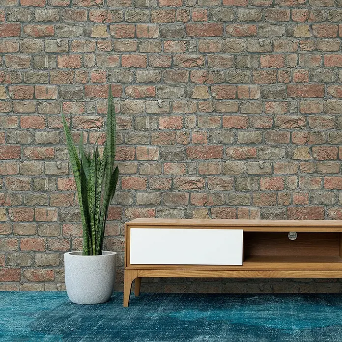 Marburg GZSZ Vliestapete Steinwand - Terra, Steinoptik, 10,05 x 0,53 m - Eine moderne TV-Bank aus Holz mit weißer Schublade, kombiniert mit einer grünen Zimmerpflanze vor einer Backsteinwand.