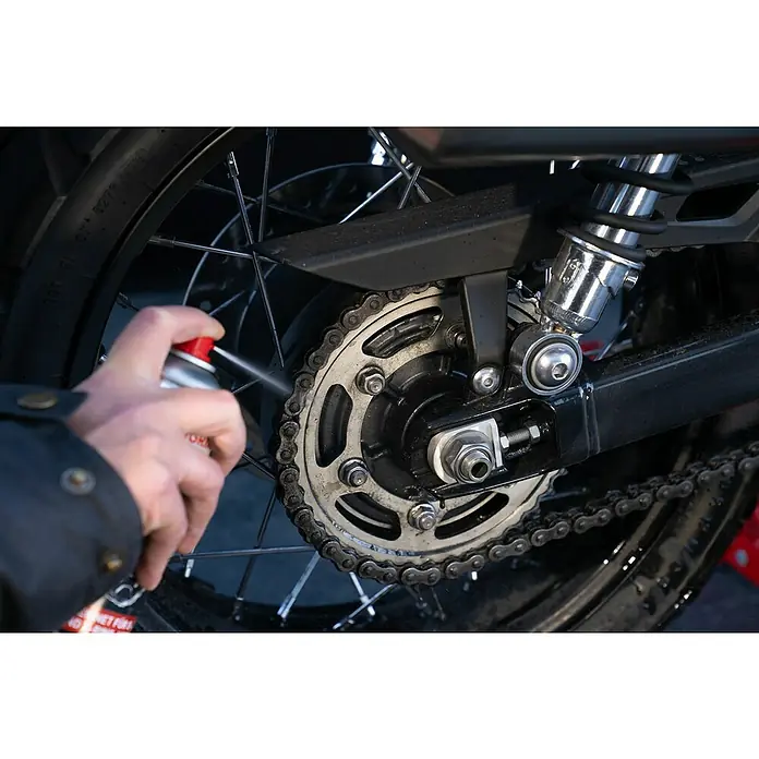 Nigrin Moto-Bike Kettenreiniger - 500 ml - Eine Nahaufnahme eines Motorrads, bei dem eine Person mit einer Sprühdose die Kette des Motorrads schmiert.