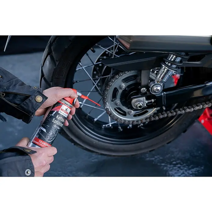 Nigrin Moto-Bike Ketten-Sprühfett Dry Lube - 400 ml - Eine Dose Nigrin Ketten-Sprühfett wird auf die Kette eines Motorrads aufgesprüht, um die Schmierung zu verbessern und die Lebensdauer zu verlängern.