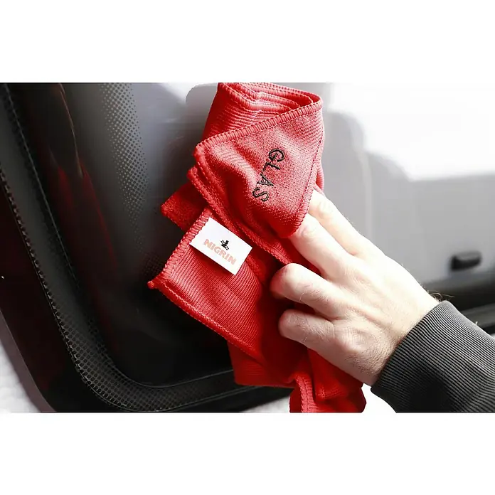 Nigrin Performance Mikrofaser-Set - 3 -tlg. - Ein rotes Nigrin-Glasreinigungstuch wird von einer Hand gehalten, um eine Autoscheibe zu putzen. Das Tuch trägt den Aufdruck "Glas".