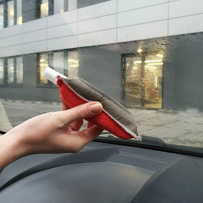 Nigrin Antibeschlagschwamm - Ausstattung: Sprühkopf - Ein Fensterreiniger mit rotem Griff wird von einer Hand gehalten, um eine beschlagene Autoscheibe zu reinigen.