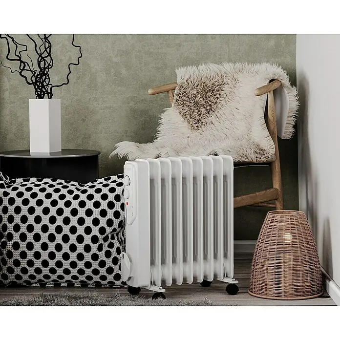 Voltomat HEATING Ölradiator - 2.000 W, Raumgröße bis ca. 20 m², Weiß - Ein weißer, tragbarer Ölradiator steht vor einem Stuhl mit einem Fell und einem schwarzen und weißen Kissen. Der Radiator ist kompakt und mobil.