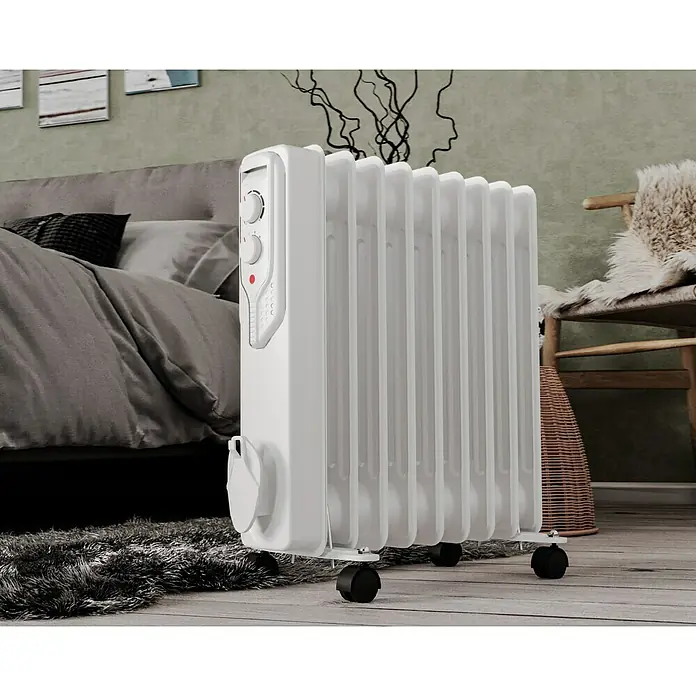 Voltomat HEATING Ölradiator - 2.000 W, Raumgröße bis ca. 20 m², Weiß - Ein weißer, tragbarer Heizkörper mit Rollen vor einem Bett und einem Stuhl. Ideal für zusätzliche Wärme im Raum.