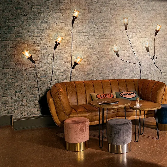 Marburg GZSZ Vliestapete Steinwand - Steingrau, Steinoptik, 10,05 x 0,53 m - Gemütliche Sitzecke mit Ledersofa, Hockern und Lampen. Die sanfte Beleuchtung sorgt für eine entspannte Atmosphäre.