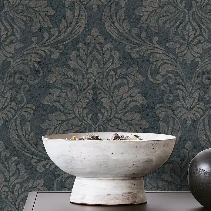 Marburg GZSZ Vliestapete - Schwarz/Braun, Ornament, 10,05 x 0,53 m - Nahaufnahme einer Dekoschale auf einem dunklen Tisch vor gemusterter Tapete, die eine elegante und stilvolle Atmosphäre erzeugt.