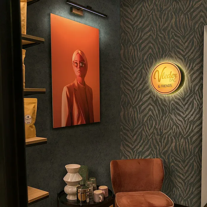 Marburg GZSZ Vliestapete Moderner Zebralook - Schwarz/Braun, Tieroptik, 10,05 x 0,53 m - Nahaufnahme eines stilvollen Interieurs mit einem beleuchteten Wandbild, einem runden Logo und einem eleganten Samtstuhl.