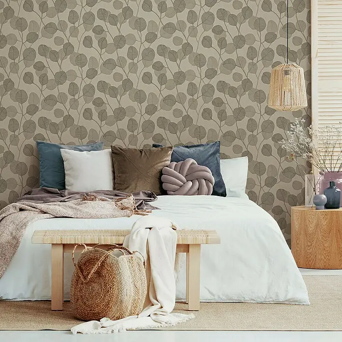 Marburg GZSZ Vliestapete Blätterranke - Beige/Braun, Floral, 10,05 x 0,53 m - Schlafzimmer mit Bett, Bank, Korb und Nachttisch in warmen Farben. Die Wand ist mit einem Blättermuster verziert.