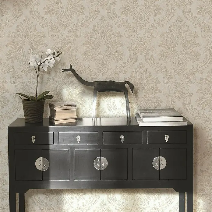 Marburg GZSZ Vliestapete - Beige, Ornament, 10,05 x 0,53 m - Schwarze Kommode mit Orchidee, Bücher und einer Tierfigur als Dekoration vor einer gemusterten Tapete.