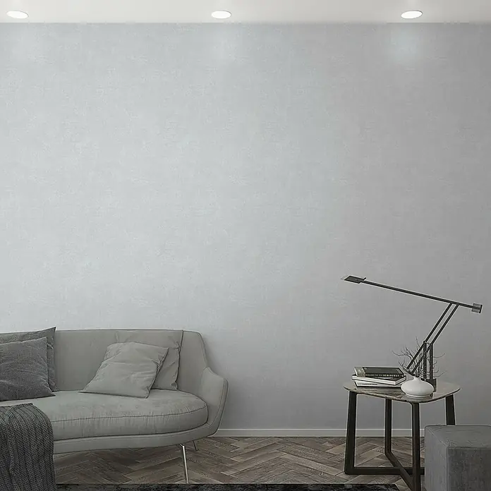 Marburg GZSZ Vliestapete - Mittleres Grau, Uni, 10,05 x 0,53 m - Graues Sofa mit Kissen, Tischlampe und Büchern auf einem Beistelltisch. Minimalistisches Wohnzimmer mit stilvoller Einrichtung und gedämpften Farben.