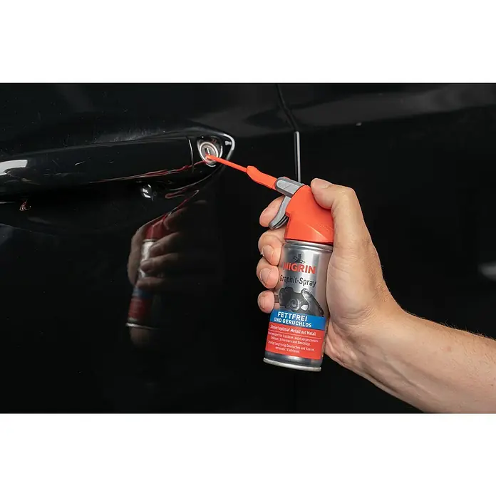 Nigrin Graphit-Spray - 100 ml - Detailaufnahme einer Hand, die NIGRIN Graphit-Spray in ein Autoschloss sprüht, um es zu schmieren und vor dem Einfrieren zu schützen.