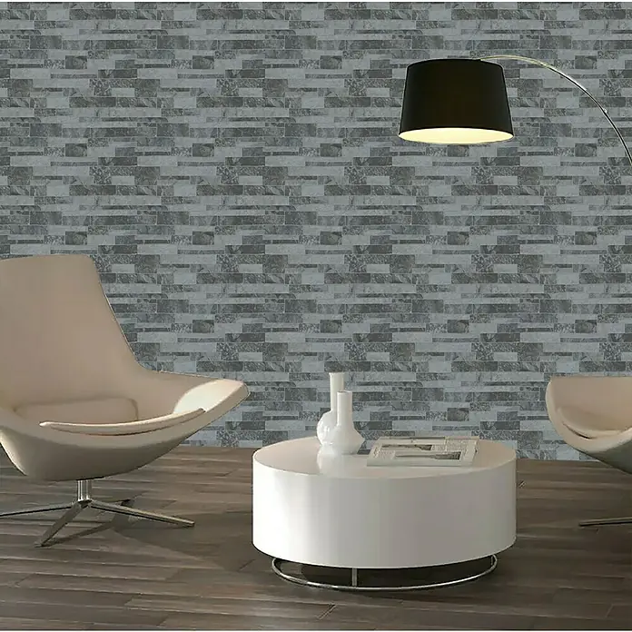 Verblendstein Durango Jet 8 - 50 x 33,3 cm, Hellgrau, Natursteinoptik - Elegantes Wohnzimmer mit einer grauen Ziegelwand, zwei Sesseln und einem runden, weißen Couchtisch. Eine Stehlampe rundet das moderne Design ab.