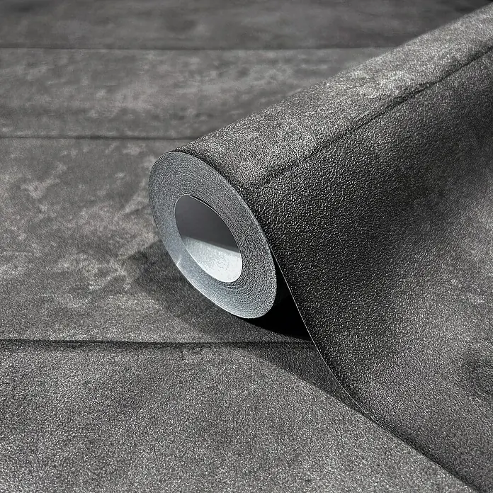 Marburg GZSZ Vliestapete - Anthrazit, Betonoptik, 10,05 x 0,53 m - Nahaufnahme einer Rolle dunkler, strukturierter Tapete, die sich teilweise abrollt und die Textur und das Design hervorhebt.