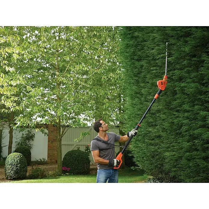 Black+Decker Cortasetos telescópico PH5551-QS - 550 W - Hombre recortando un seto alto con un cortasetos de pértiga inalámbrico Black+Decker para jardín.