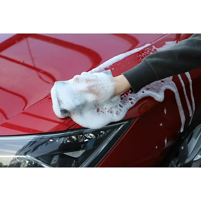 Nigrin Auto-Shampoo Konzentrat - 1 l, Orangenduft - Ein rotes Auto wird mit einem schaumigen Schwamm gewaschen, um die Karosserie zu reinigen und den Lack zu pflegen.