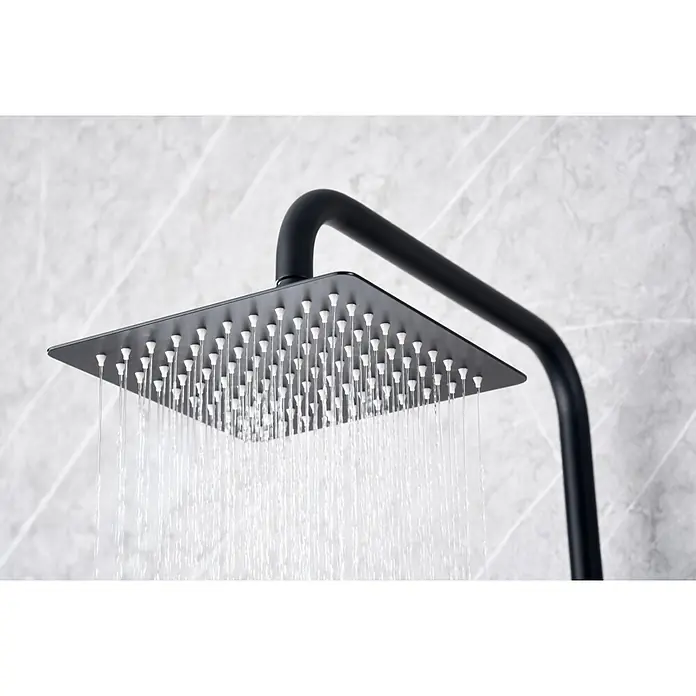 Imex Art Sistema de ducha - Grifo termostático, Negro - Primer plano de un cabezal de ducha cuadrado y negro que rocía agua desde muchas boquillas pequeñas, montado en un accesorio negro contra una pared de mármol.