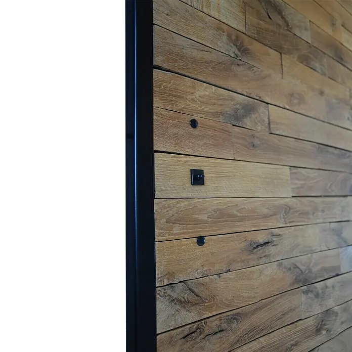 Kornik Griff Loft Slim - Schwarz, 183 x 20 mm - Nahaufnahme einer Holzwand mit stilvollen Akzenten. Die Wand weist eine dunkle Umrandung, rustikale Textur und dekorative Elemente auf.