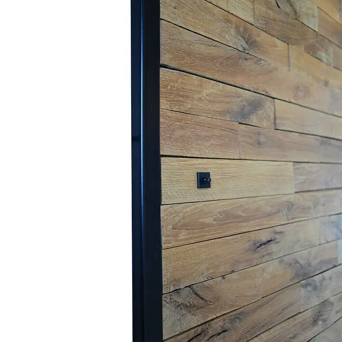 Kornik Griff Loft Slim - Schwarz, 183 x 20 mm - Nahaufnahme einer Holzwand mit Metallrahmen und schwarzer Befestigung, die modernes Design und rustikalen Charme vereint.