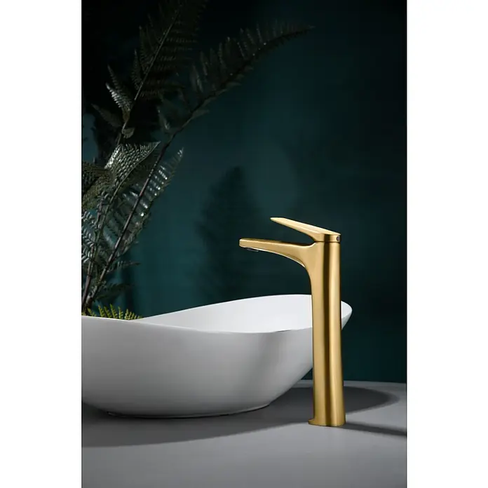 Imex Delos Grifo de lavabo alto - Oro - Elegante grifo dorado de baño frente a un lavabo blanco con un fondo oscuro. El grifo es un punto de atracción en el baño moderno.