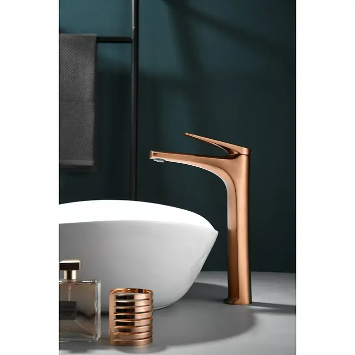 Imex Delos Grifo de lavabo alto - Oro rosa - Elegante grifo de baño en oro rosa junto a un lavabo blanco con elegantes accesorios de baño para un diseño moderno.