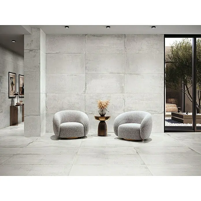 Feinsteinzeugfliese Bond - 60 x 120 cm, Weiß, Matt - Zwei graue Sessel und ein Beistelltisch auf einem gefliesten Boden vor einer Betonwand. Modernes Design für Wohnräume.
