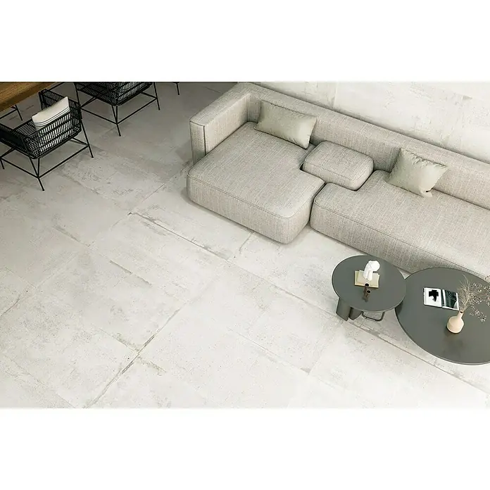 Feinsteinzeugfliese Bond - 60 x 120 cm, Weiß, Matt - Ein helles Wohnzimmer mit modernen Möbeln, darunter ein graues Sofa und Couchtische, auf einem strukturierten, weißen Bodenbelag.