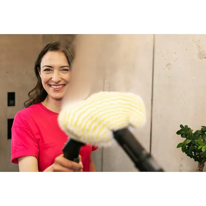 Kärcher Dampfreiniger SC 2 EasyFix - 1.500 W, Aufheizzeit: 6,5 min, Behältervolumen: 1 l - Frau lächelt und hält einen Dampfreiniger mit gelbem und weißem Bezug in die Kamera, der Dampf abgibt.