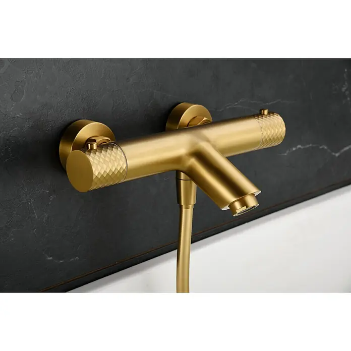 Imex Génova Grifo monomando de bañera - oro - Grifo dorado con manijas moleteadas, con un diseño moderno, montado en una pared de mármol oscuro.