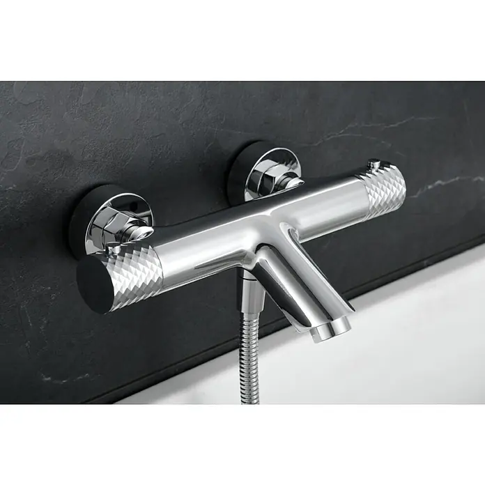 Imex Génova Grifo monomando de bañera - Cromo, Resplandeciente - Primer plano de un elegante grifo de bañera cromado con manijas texturizadas, montado en una pared oscura, que muestra un diseño moderno y una artesanía de alta calidad.