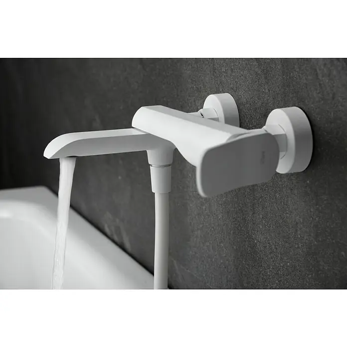 Imex Dinamarca Grifo monomando de bañera - Profundidad del grifo: 20,2 cm, Blanco, Mate - Primer plano de un moderno grifo blanco con agua corriendo, montado en una pared oscura. Diseño elegante para el baño.