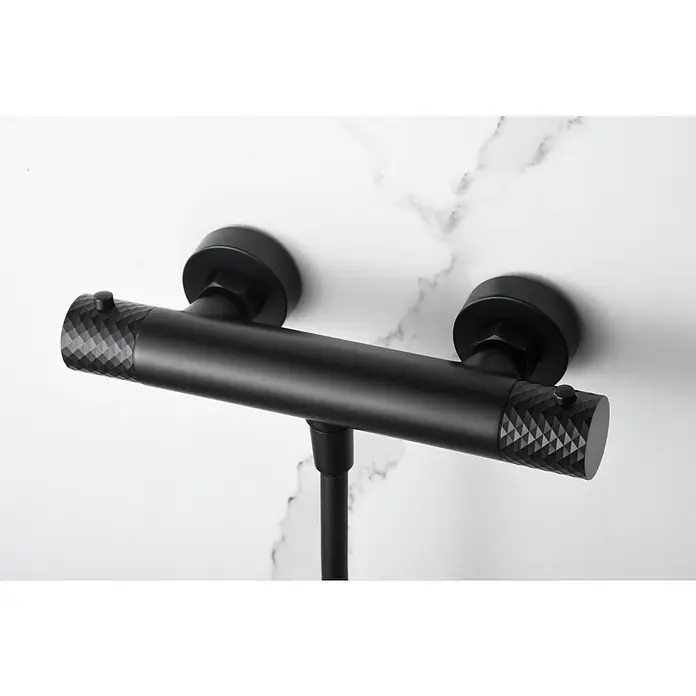 Imex Génova Grifo con termostato - Ancho: 29,5 cm, Negro, Mate - Un accesorio de ducha negro con un patrón de diamantes en los extremos, montado en una pared de mármol blanco.