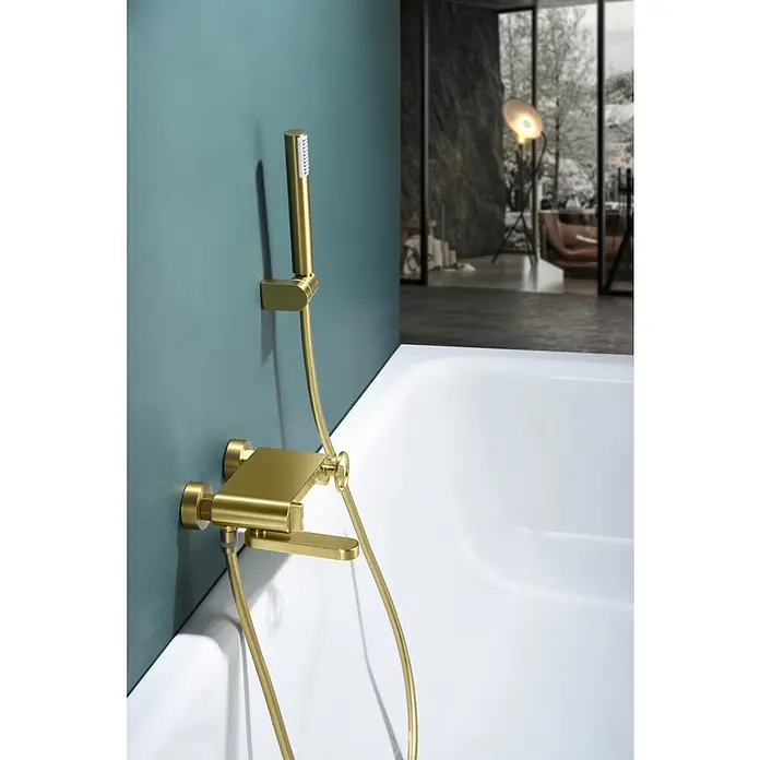 Imex Olimpo Grifo monomando de bañera - Oro cepillado - Primer plano de un grifo dorado de bañera sobre una pared verde azulado, destacando el diseño moderno y los detalles lujosos en el baño.