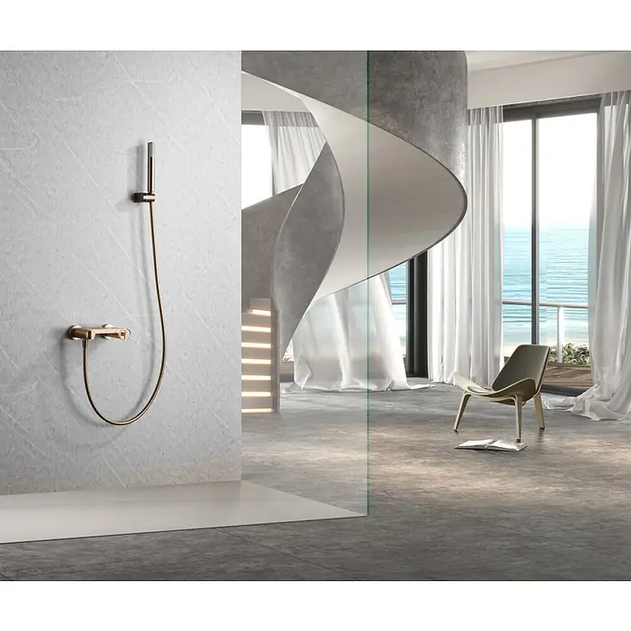 Imex Olimpo Grifo de ducha - Oro rosa - Moderno accesorio de baño de aspecto dorado en una pared de mármol gris, separado por vidrio de una elegante habitación con vistas al mar.